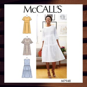 May include: McCall's sewing pattern M7948 for a tiered dress with different sleeve and neckline options. The pattern includes four different dress styles: a yellow dress with short sleeves, a floral dress with short sleeves and ruffles, a blue and white gingham dress with no sleeves, and a white eyelet dress with 3/4 sleeves.