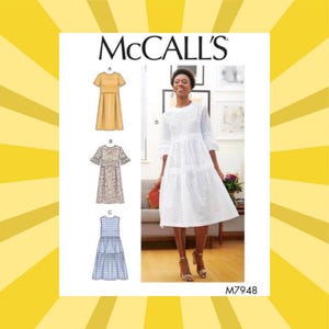 May include: McCall's sewing pattern M7948 featuring three dress designs. The image shows a woman wearing a white eyelet dress. The pattern includes a yellow dress, a floral dress, and a blue and white checkered dress. The background is yellow with white rays.
