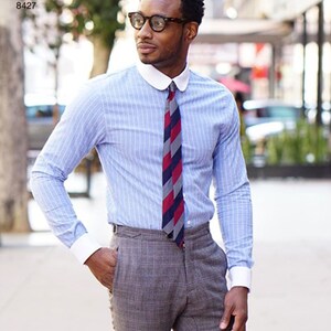 May include: A light blue striped dress shirt with a white collar and cuffs, paired with a patterned tie and gray plaid trousers. The shirt is buttoned up and the tie is knotted. The image also shows a Simplicity Pattern 8427.