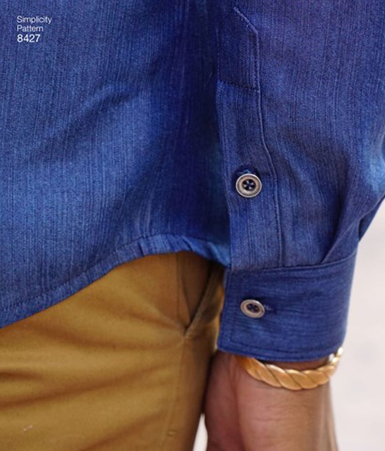 May include: Close-up of a blue denim shirt sleeve with two buttons. The cuff is buttoned. The shirt is paired with tan pants. The text "Simplicity Pattern 8427" is visible in the upper left corner.