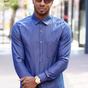 May include: A long-sleeved, denim-style blue shirt with a button-down front and a chest pocket. The shirt is paired with a gold watch and sunglasses. The text "Simplicity Pattern 8427" is visible in the upper left corner.