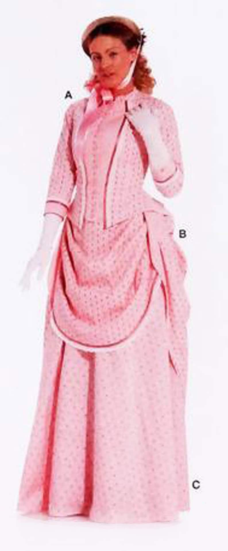 May include: A pink vintage dress with a dotted pattern, long sleeves, and a draped skirt. The dress features a high neckline, a bow, and white gloves. A matching hat completes the ensemble.
