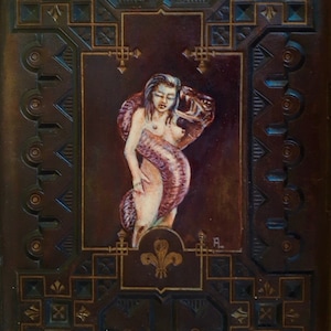 以下が含まれることがあります： 装飾的な濃い茶色のフレームの中に描かれた、蛇に抱きしめられた女性の油絵。 女性は長い髪をしており、裸です。 蛇は彼女の体に巻き付いています。 フレームは金色のアクセントが付いた幾何学模様です。