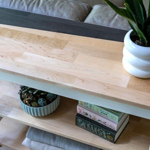 a wooden table with a white vase containing a potted plant, a stack of books, and a blue bowl filled with succulents.