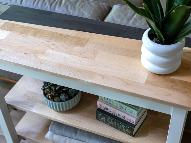 a wooden table with a white vase containing a potted plant, a stack of books, and a blue bowl filled with succulents.
