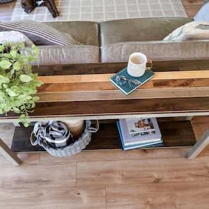 a cozy living room with a wooden coffee table in the center, adorned with various items such as a plant, a mug, a book, and a basket. The table is situated on a hardwood floor, and there is a couch in the background.