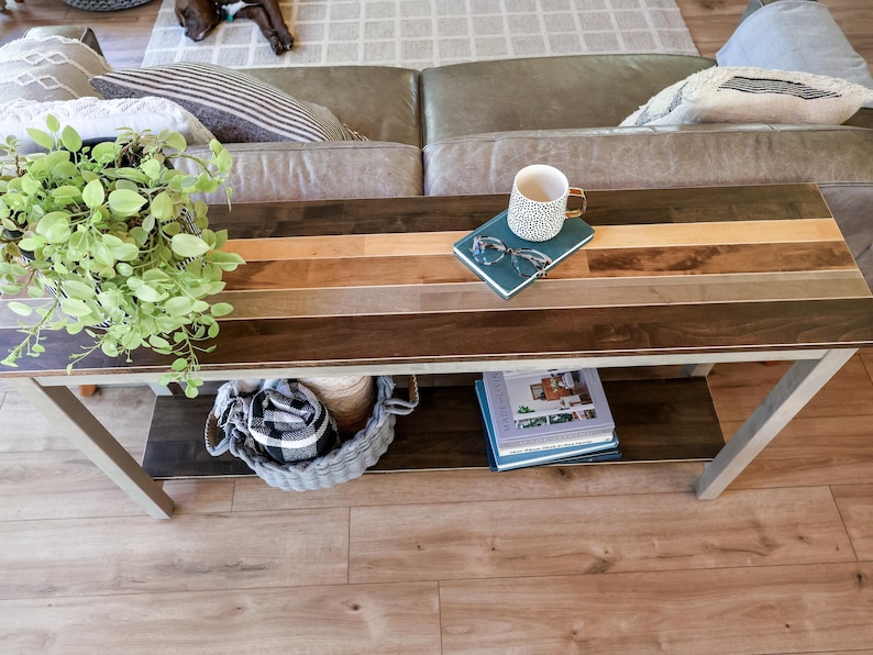 a cozy living room with a wooden coffee table in the center, adorned with various items such as a plant, a mug, a book, and a basket. The table is situated on a hardwood floor, and there is a couch in the background.