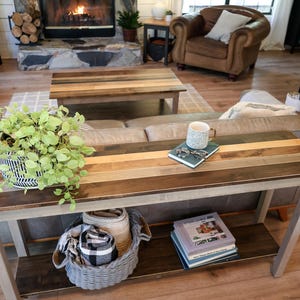 a cozy living room with a fireplace, a wooden coffee table, and a comfortable couch. The coffee table has a plant, a mug, and some books on it, creating a welcoming atmosphere.