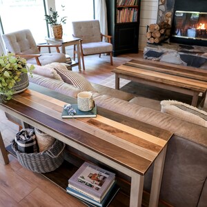a cozy living room with a fireplace, wooden furniture, and a large window. The room is furnished with a sofa, chairs, and a coffee table. There are also decorative elements such as potted plants and books, creating a warm and inviting atmosphere.
