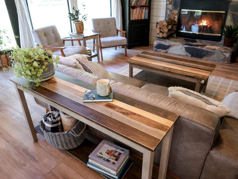a cozy living room with a fireplace, wooden furniture, and a large window. The room is furnished with a sofa, chairs, and a coffee table. There are also decorative elements such as potted plants and books, creating a warm and inviting atmosphere.