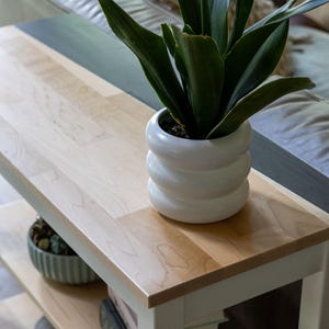 A potted plant with long, thin leaves sits on a wooden side table, accompanied by a white vase and a small bowl.