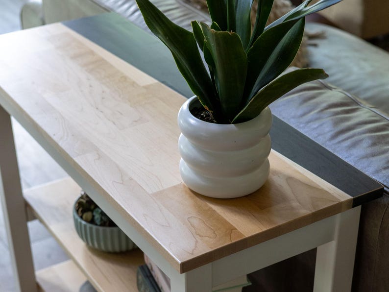 A potted plant with long, thin leaves sits on a wooden side table, accompanied by a white vase and a small bowl.
