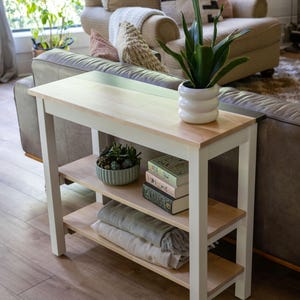 a cozy living room with a white side table, a sofa, and various decorative items such as a potted plant, books, and a bowl.