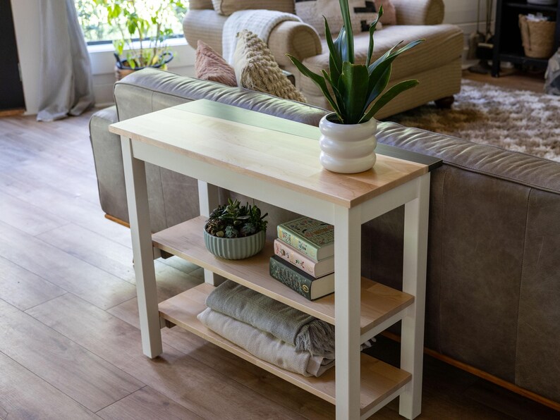 a cozy living room with a white side table, a sofa, and various decorative items such as a potted plant, books, and a bowl.