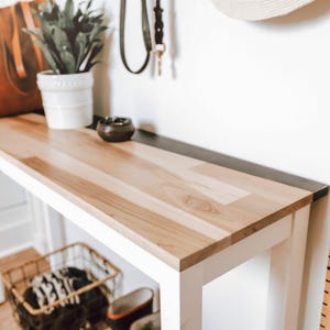 a wooden console table with a white top, a potted plant, a leather bag, a small bowl, and a metal ruler on the wall next to it.