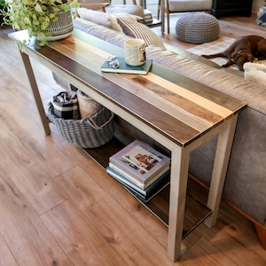 a cozy living room with a wooden console table, a gray sofa, and a brown dog resting on the floor. The table has a striped top and is decorated with various items, including a plant, a coffee cup, and a stack of books.