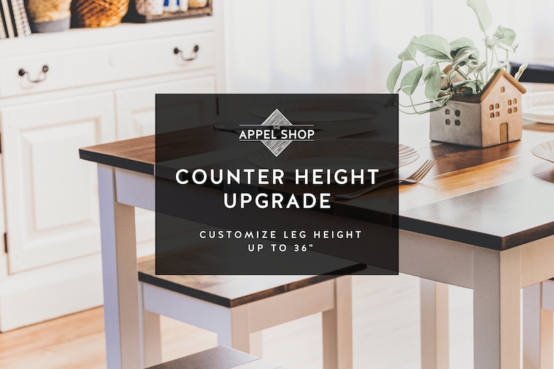May include: A white table with a wood top and a black sign that says "Counter Height Upgrade" with the text "Customize Leg Height Up To 36" underneath. The table is set with a place setting and a potted plant.