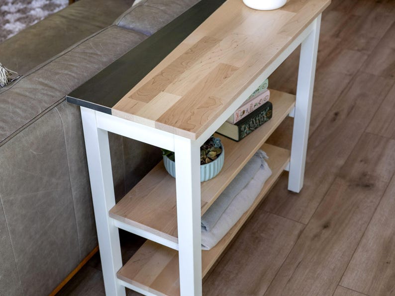 a modern, minimalist living room with a white side table and a gray couch. The table has a wooden top and metal frame, and it has two shelves for storage. The couch is positioned next to the table, creating a cozy and functional seating area.