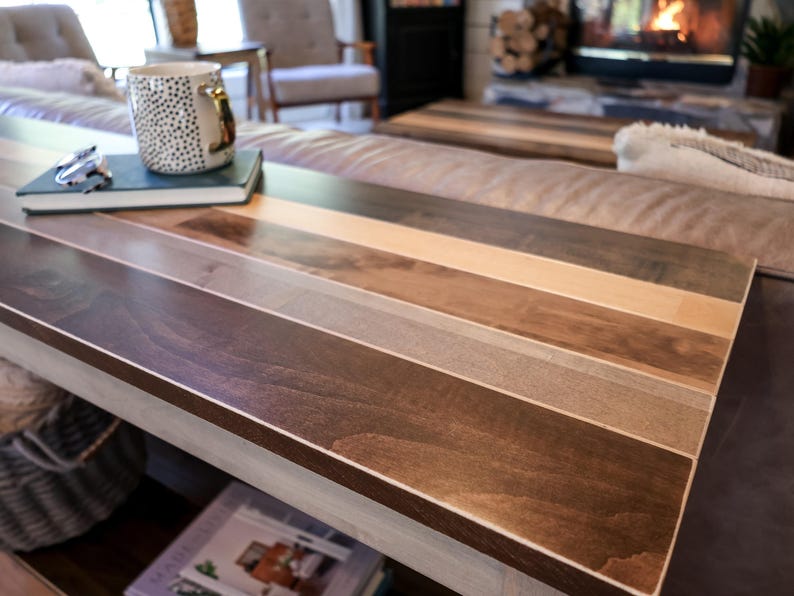 a wooden coffee table with a striped pattern, featuring a white mug and a book on top. The table is situated in a living room with a couch and a fireplace visible in the background.
