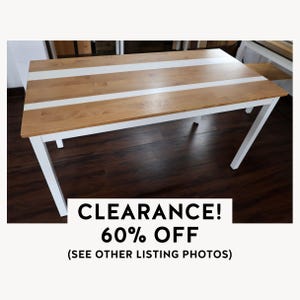May include: A rectangular wooden table with a light brown tabletop and two white stripes running lengthwise. The legs are white. The text "CLEARANCE! 60% OFF" is at the bottom of the image.