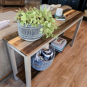 a cozy living room with a wooden coffee table, a comfortable couch, and a potted plant on the table. The table has a shelf underneath it, providing storage space. There are also some books and a basket on the table, adding to the homely atmosphere.
