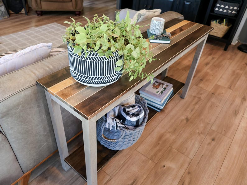 a cozy living room with a wooden coffee table, a comfortable couch, and a potted plant on the table. The table has a shelf underneath it, providing storage space. There are also some books and a basket on the table, adding to the homely atmosphere.