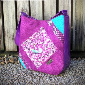 Puede incluir: Un bolso tote morado y turquesa con un estampado floral que presenta un zorro. El bolso mide 28 cm de ancho por 31 cm de alto por 7,6 cm de profundidad. El texto "Feature Me Everyday Tote" está en la parte superior de la imagen.
