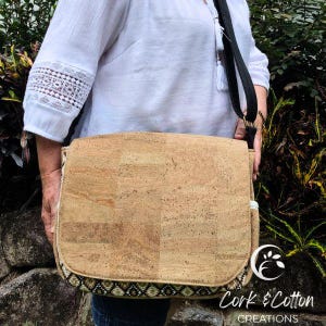 May include: A brown cork messenger bag with a black adjustable strap and a patterned trim. The bag is made by Cork & Cotton Creations.