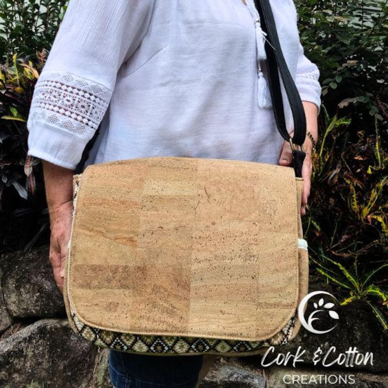 May include: A brown cork messenger bag with a black adjustable strap and a patterned trim. The bag is made by Cork & Cotton Creations.