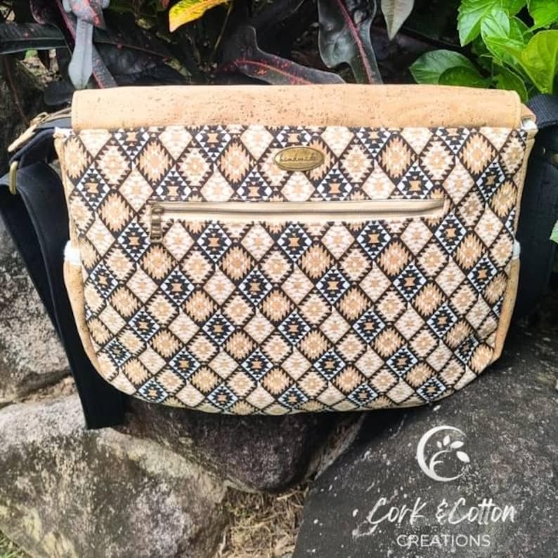 May include: A brown and black patterned cork and cotton messenger bag with a zipped pocket and a gold metal tag that says "handmade".