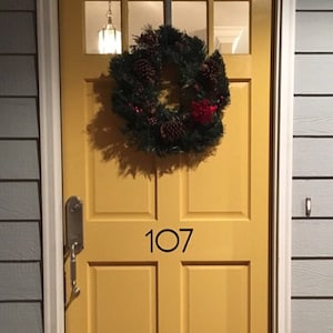 May include: A yellow door with a Christmas wreath and the number 107 on it.