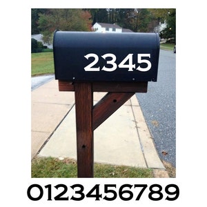 Peut inclure: Une boîte aux lettres noire avec les chiffres blancs "2345" affichés. La boîte aux lettres est montée sur un poteau en bois. Les chiffres 0 à 9 sont affichés en dessous.