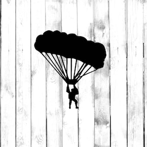 May include: Silhouette of a skydiver with a parachute open, descending against a white wood background.