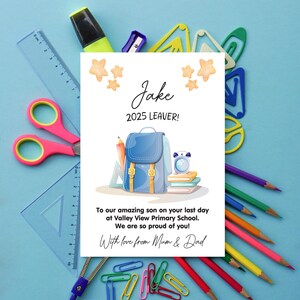 Op de afbeelding: Een gepersonaliseerde kaart voor Jake, een afgestudeerde in 2025, met een blauwe rugzakillustratie, potloden en tekst. De kaart is omgeven door schoolspullen zoals scharen, linialen en paperclips op een blauwe achtergrond.
