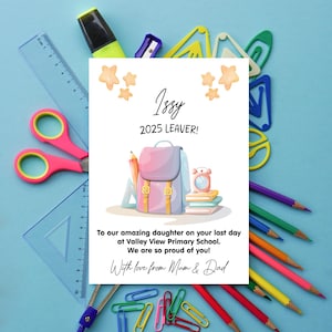 Op de afbeelding: Een wenskaart voor "Issy" met de tekst "2025 LEAVER!" en een schoolthema-illustratie. De kaart is omgeven door schoolbenodigdheden zoals potloden, scharen en paperclips op een blauwe achtergrond.