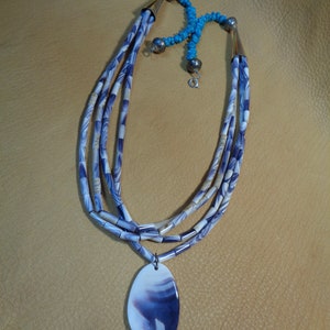 May include: A multi-strand necklace made of purple and white shell beads with a large purple and white shell pendant.