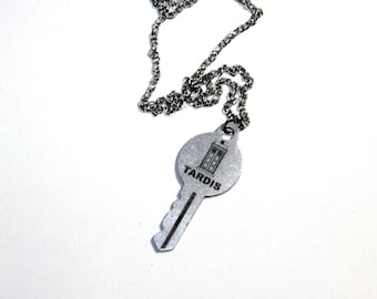 May include: A silver key necklace with a round pendant featuring a TARDIS silhouette and the word "TARDIS" printed on it.