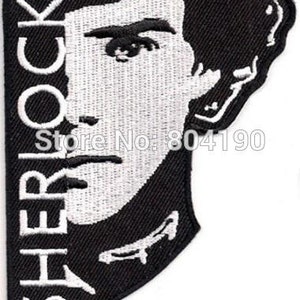 May include: Black and white embroidered patch featuring a portrait of Sherlock Holmes with the name "SHERLOCK" in white capital letters. The patch has a unique, irregular shape.