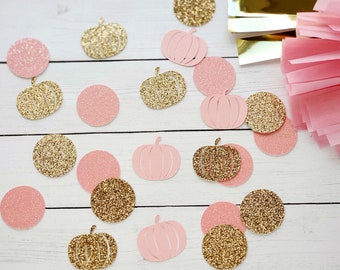 May include: Pink and gold glitter confetti with pumpkin shapes and circles. The confetti is scattered on a white wooden surface.
