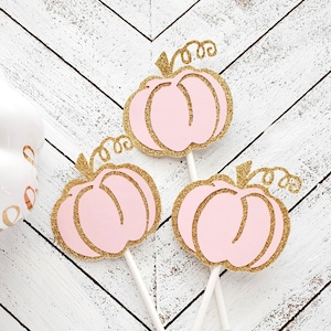 May include: Three pink and gold glitter pumpkin cupcake toppers with white sticks.