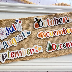Puede incluir: Un conjunto de pegatinas de calendario mensuales ilustradas y coloridas con un tema festivo. Las pegatinas representan los meses de julio, agosto, septiembre, octubre, noviembre y diciembre. Cada mes tiene un dise&ntilde;o &uacute;nico con un esquema de color e ilustraci&oacute;n diferentes.