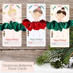 Puede incluir: Tarjetas de recuerdo de bailarina navideña con ilustraciones de bailarinas con tutús rosas. Cada tarjeta se combina con una cinta para el pelo verde o roja. Las tarjetas tienen el texto "Happy Holidays! Love," y un espacio para un nombre.