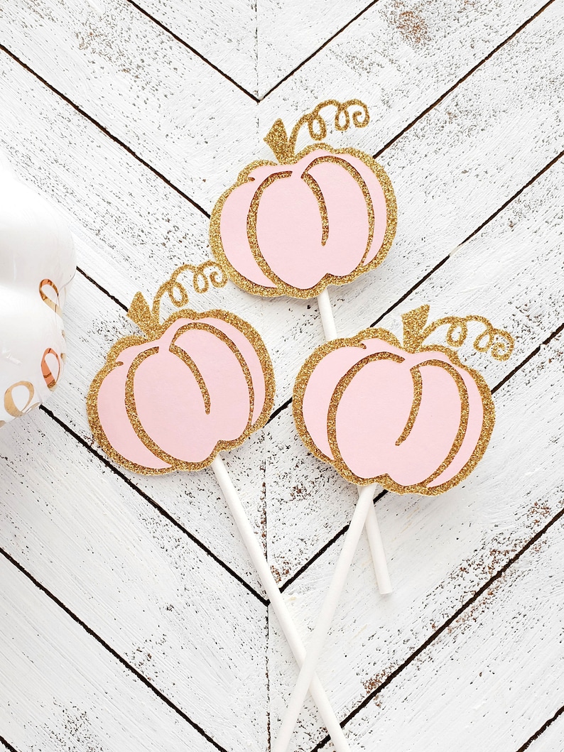 May include: Three pink and gold glitter pumpkin cupcake toppers with white sticks.