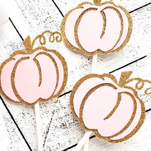 May include: Three pink and gold glitter pumpkin cupcake toppers with white sticks.
