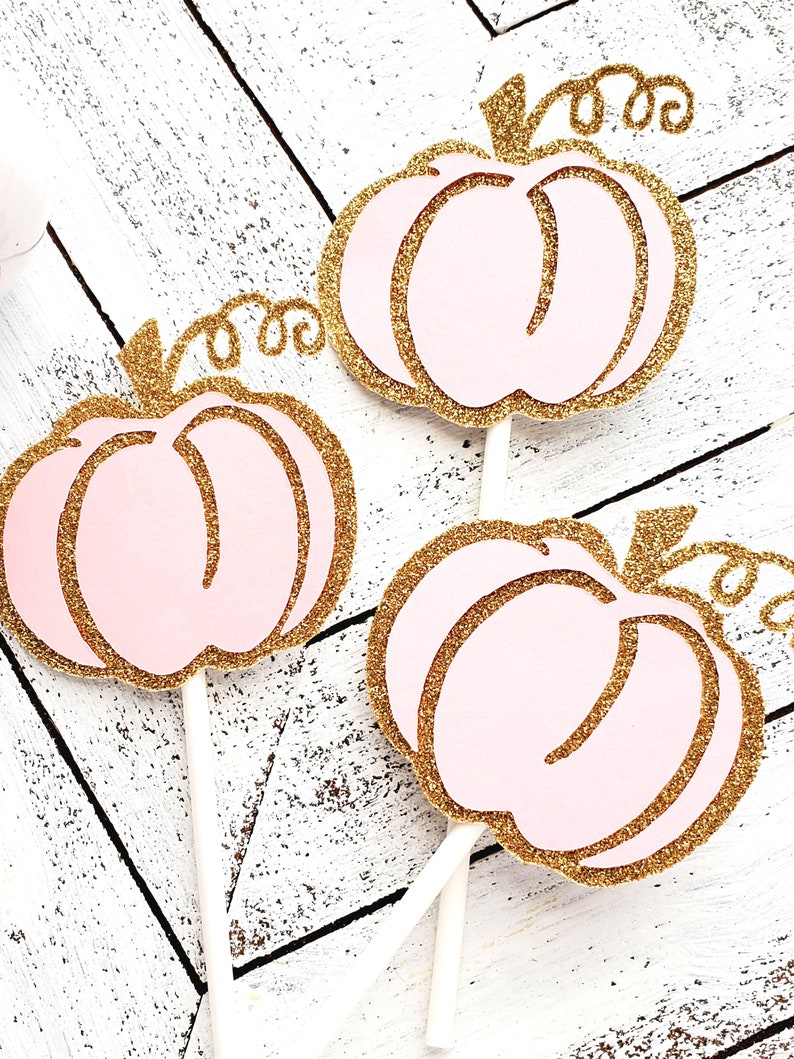 May include: Three pink and gold glitter pumpkin cupcake toppers with white sticks.