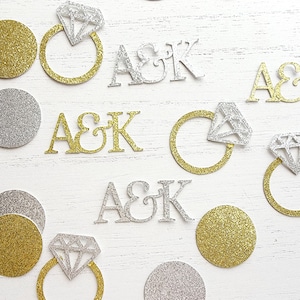 May include: Gold and silver glitter confetti with the letters A & K, a ring with a diamond, and circles. The confetti is perfect for a wedding or engagement party.