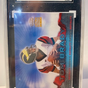 Könnte beinhalten: Eine bewertete Tom Brady Rookie-Karte aus dem Set Pacific Crown Royale aus dem Jahr 2000. Die Karte ist in nahezu neuwertigem Zustand und hat eine Bewertung von 7,5. Die Karte zeigt ein Foto von Brady in seinem Trikot der Michigan Wolverines.