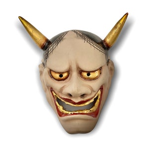 May include: A traditional Japanese demon mask with gold horns, black and white painted details, and red and gold painted lips. The mask has a menacing expression with large, yellow eyes.