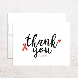 May include: A white card with a matching envelope. The card features the words "thank you" in black script, a red ribbon, a red heart, and the name "EMMA" in a smaller font.