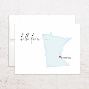 May include: A white greeting card with a light blue watercolor map of Minnesota. The card features the text "hello from" in elegant script, with "Minneapolis" and a red heart marking the city's location.